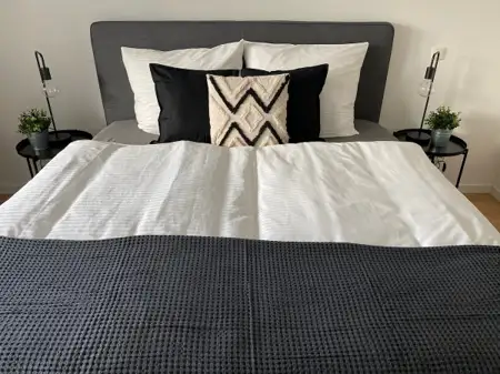 Modernes Schlafzimmer mit einem Bett, weißen und schwarzen Kissen sowie einer dekorativen Decke in Grau.