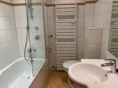 Modernes Badezimmer mit Badewanne, Dusche und Waschbecken in hellen Fliesen.